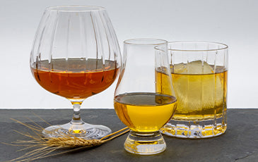 Three Glasses of Bourbon and piece of wheat on a Slate counter with a white background.