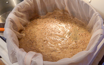 Crushed grains steeping in a mesh brew bag during a cold mash at room temp