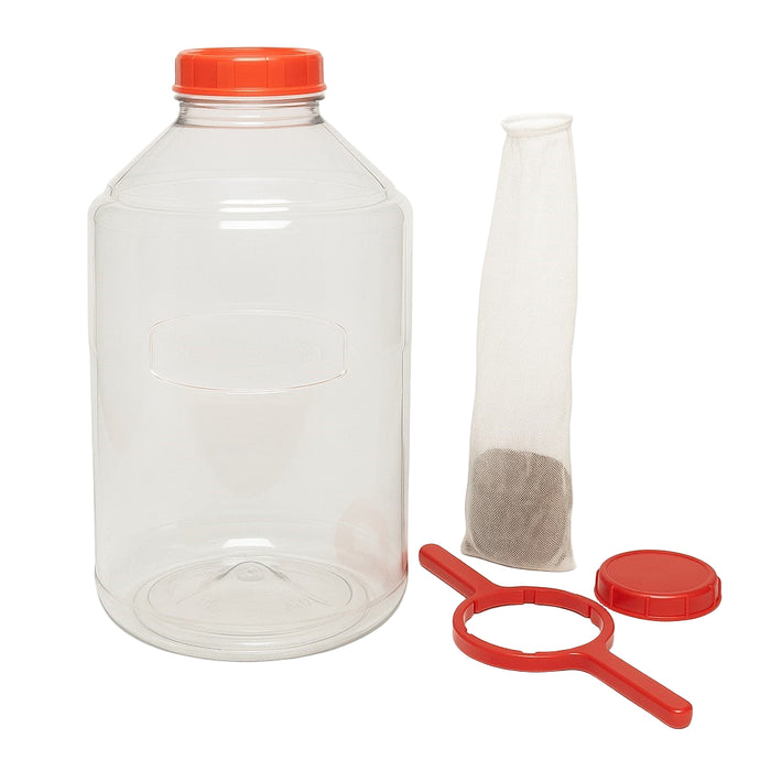 6-gallon clear FerMonster fermenter with red lid shown alongside included accessories — mesh straining bag, red lid wrench, and solid replacement lid — displayed on a clean white background.