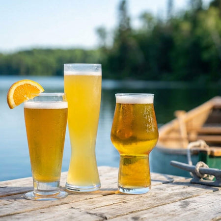 Three glasses of beer on a wooden dock with a lake and trees in the background