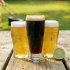 Three glasses of beer on a wooden table with a blurred outdoor background