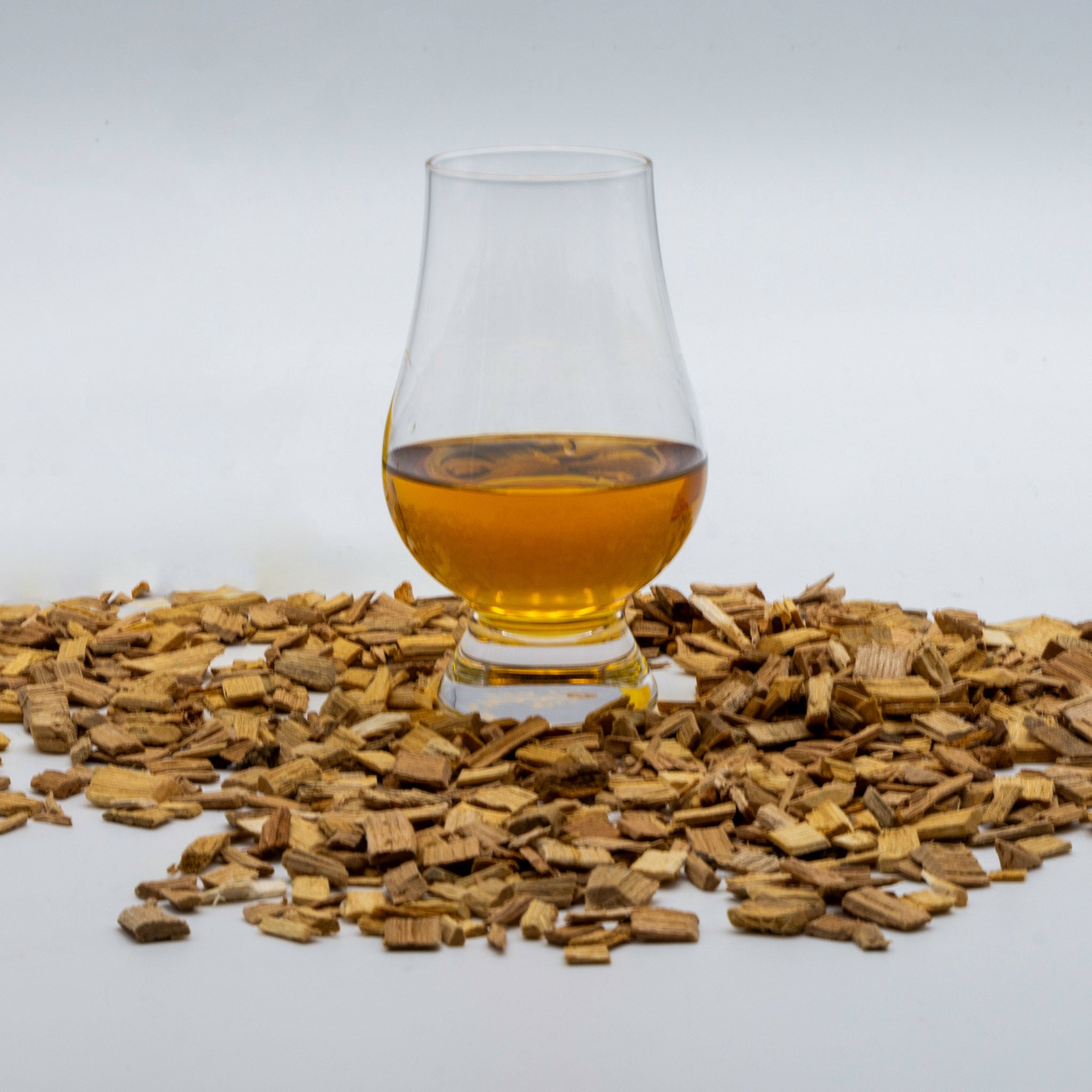 Aged rum in a glass with wood chip around it.