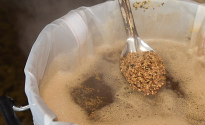 Spoon with grain in a kettle of wort.