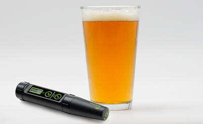 Digital thermometer next to a glass of beer on a white background