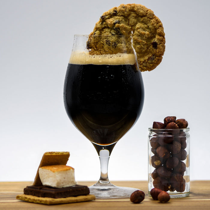 Pastry Stout homebrew in a glass with an oatmeal cookie wedge, next to a cup of hazelnuts and a fully-assembled smores bar
