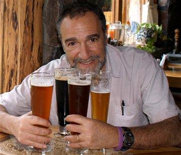 A smiling man with four beers of various styles.